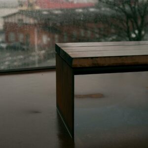 A sleek bench sits indoors against a rainy window, reflecting a muted urban scene outside.